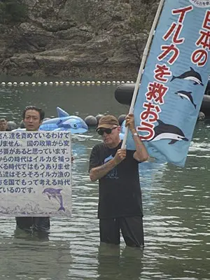 Ric O'Barry (dir.) ergue cartaz em japonês: 'Salvem os golfinhos no Japão', ao lado do ativista japonês Satoshi Komiyama (Foto: Dolphin Project/AP)