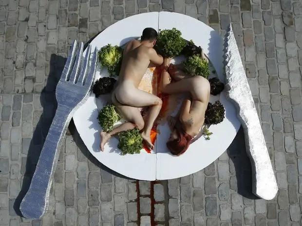 Casal 'se serve' nu em um prato gigante em protesto promovendo o vegetarianismo no centro de Barcelona, na Espanha. (Foto: Albert Gea/Reuters)
