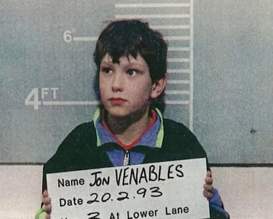 uma criança segurando uma placa de identificação. seu nome é Jon Venables. o menino cometeu crimes de crueldade contra animais.